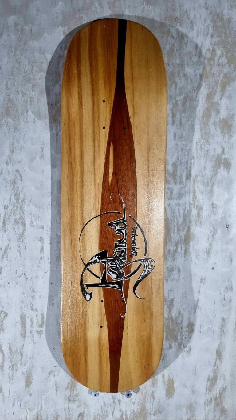 planche de skate avec liseret de marquetterie d'acajou et calligraphie Pyébwa bichromatique.
